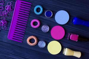 Colorful and bright cosmetics. Beauty care tools. Beauty salon. Girl's paradise. Nail polishes, sequins, pink hair bands and comb on a dark blue wooden desk. Bright still life of beauty instruments. photo