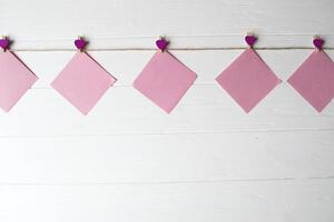 Pink memo sheets fastened with a decorative pin on a white wooden board. photo