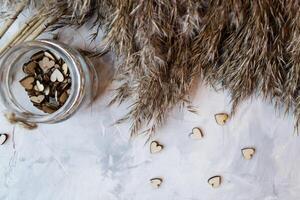 Wooden hearts in a jar and bulrush plant on a grey textured background. Stylish still life. photo