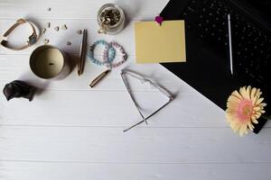 Laptop, colorful memo sheets, eyeglasses, stylus, pink gerbera and elements of decoration on a white wooden work desk. Beautiful female workplace top view. photo