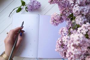 lila y bloc en un blanco escritorio. mujer es escritura en un cuaderno. parte superior vista. foto