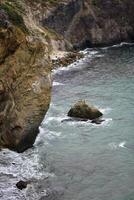 three seabirds all sit on a stone in the sea during a storm in cloudy weather among the rocks photo