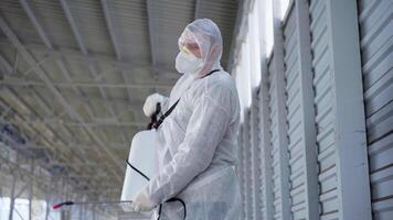 a man in a protective suit and mask with a water spraying tool standing in an empty parking lot video