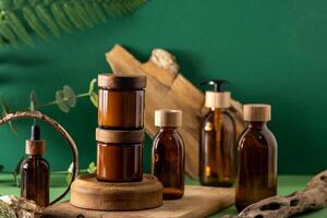 Glass brown containers for cosmetics with wooden lids. Cream, dropper bottle and lotion. Green background. Care and beauty. Bottles. photo