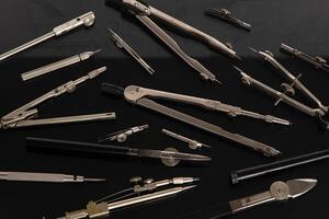 Set of old different compasses. Retro metal compasses and drafting tools on a black background. Drawing pen. photo