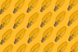 Yellow background. Electric light bulbs pattern. An old glass electric light bulb with a tungsten filament. The concept of electricity consumption and saving. photo