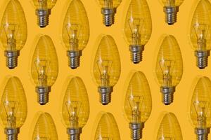 Yellow background. Electric light bulbs pattern. An old glass electric light bulb with a tungsten filament. The concept of electricity consumption and saving. photo