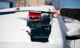 A young man wearing black warm suit for cleans his car after a snowfall on a sunny, frosty day. photo