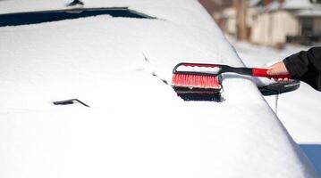 A young man wearing black warm suit for cleans his car after a snowfall on a sunny, frosty day. photo