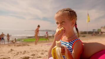 un pequeño niña comiendo un plátano en el playa video