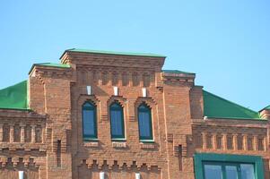 Part of an old red brick house. Restored facade with windows and stepped roof. photo
