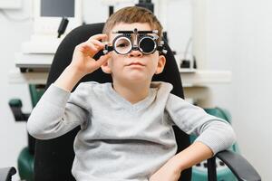 Cheerful child boy in glasses checks eye vision pediatric ophthalmologist photo