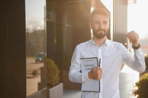 Real estate agent holding key on blurred background, closeup photo