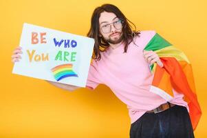 Gay man wearing bright pink top hold rainbow striped flag isolated on colored background studio portrait. People lifestyle fashion lgbtq concept photo