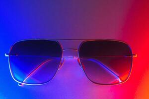 Stylish sunglasses shot using pink and blue abstract colored lighting with copy space. photo