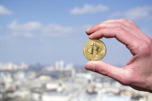 Golden bitcoin in male hand on blurred city background. Man holding a coin of cryptocurrency. photo