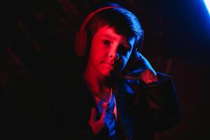 Studio shot in dark studio with neon light. Portrait of a stylish boy with headphones photo
