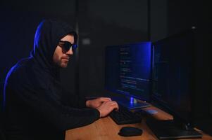 hacker sentado a escritorio en oscuro atmósfera. un computadora programador o hacker anónimo computadora hacker foto