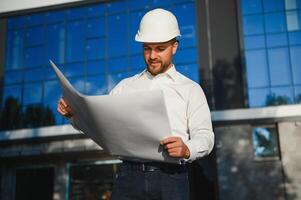 Engineer next to building cranes. Concept - large construction project. Architect directs the construction process. Drawings and tablet in the hands. photo