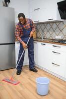 joven africano hombre lavados el piso con un fregona en el habitación foto