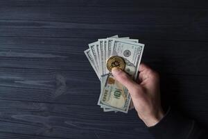 Golden bitcoin and dollars in male hand on a dark blue wooden background. Gold coin of cryptocurrency. photo