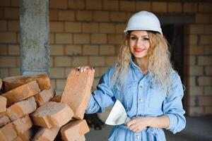 Attractive female construction worker in hardhat. Confident young specialist in checkered blue shirt in jeans standing in empty room. Interior design and renovation service photo