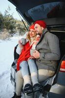 Smiling together. Nice couple have weekend at countryside at winter time. Sitting on the rear part of modern car. photo