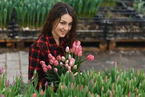 Young beautiful woman greenhouse worker holds a blooming tulips in her hands and smiles. photo