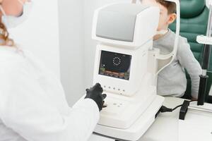 Optometry concept. Female optometrist optician doctor examines eyesight of child boy in eye ophthalmological clinic. photo