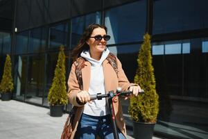 Young beautiful woman riding an electric scooter to work, modern girl, new generation, electric transport, ecology, ecological transport, sunset, electric skateboard. photo