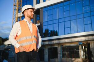 Engineer next to building cranes. Concept - large construction project. Architect directs the construction process. Drawings and tablet in the hands. photo