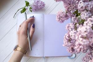lila y bloc en un blanco escritorio. mujer es escritura en un cuaderno. parte superior vista. foto