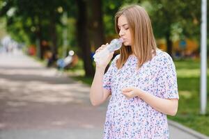 Pregnant woman stands in the park with a bottle of water. copy space photo