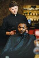 visitando peluquería. africano americano hombre en un elegante Barbero tienda foto