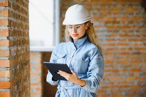 Absorbed in the work of a woman engineer working with a tablet on the background of the construction site. Portrait of a young architect, protective equipment. Selective focus photo