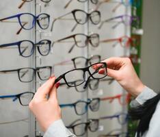 Row of glasses at an opticians. Eyeglasses shop. Stand with glasses in the store of optics. Woman's hand chooses spectacles. Eyesight correction photo