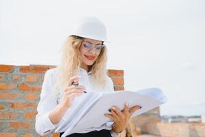construcción ingeniero. niña con construcción documentación. un mujer en un blanco difícil sombrero en contra el techo de un edificio. construcción de un nuevo casa foto