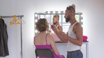 trucco artista applicare rendere su per donna chi nel davanti di specchio. barbuto gay professionale trucco artista su dietro le quinte a opera. video