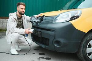 hombre participación poder cargando cable para eléctrico coche en al aire libre coche parque. y él s yendo a conectar el coche a el cargando estación en el estacionamiento lote cerca el compras centrar foto