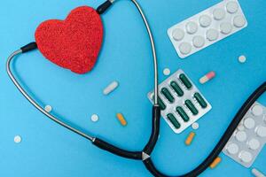 Close-up of a heart and a stethoscope on a blue background, top view. Global health care concept. caring for heart health. treatment with tablets and ampoules. photo