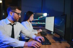 equipo de corredores de bolsa son teniendo un conversacion en un oscuro oficina con monitor pantallas foto