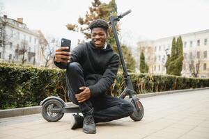 lleno cuerpo lado retrato contento africano americano hombre en móvil scooter en calle foto