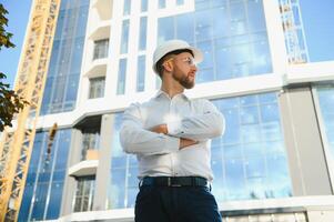 Engineer next to building cranes. Concept - large construction project. Architect directs the construction process. Drawings and tablet in the hands. photo