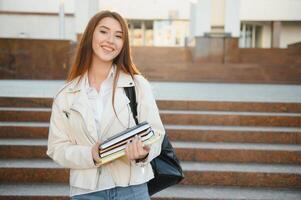 Portrait of a cheerful young girl student with backpack sitting on steps outdoors, reading book photo