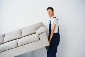 Loader moves sofa, couch. worker in overalls lifts up sofa, white background. Delivery service concept. Courier delivers furniture in case of move out, relocation. photo