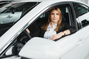 joven hermosa mujer demostración su amor a un coche en un coche sala de exposición. foto