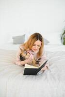 A woman reading a book and smiling as she sits in bed. The alarm clock on the desk beside her. photo