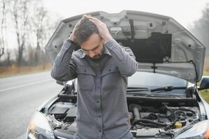 Sad driver holding his head having engine problem standing near broken car on the road. Car breakdown concept photo