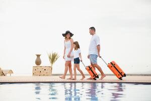 Young couple going to hotel through swimming pool upon arrival, looking for room, holding suitcases photo