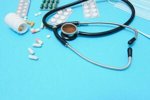 colorful tablets and capsules in a box, thermometer, statoscope, antiseptic bottle, container, tablets in a package, are located around the perimeter of the image on blue background. photo